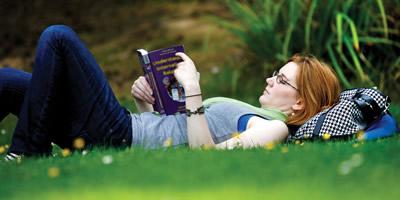Student lying on grass reading a book