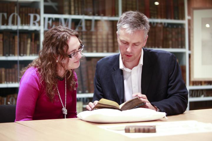 University staff showing a student a rare book in a library. 