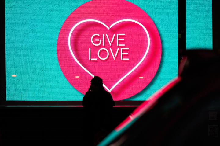 Blue and pink neon advertising sign with the words Give love inside a heart, which is inside a bigger circle