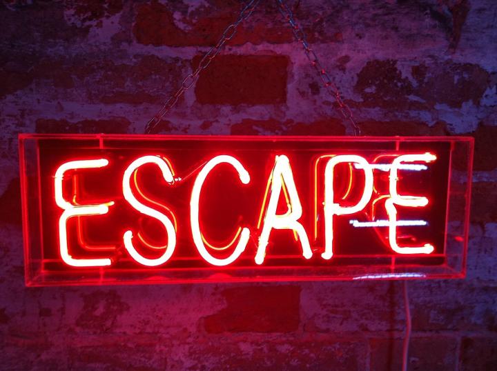 Red neon sign with the word: Escape. The sign is hanging on a brick wall. 
