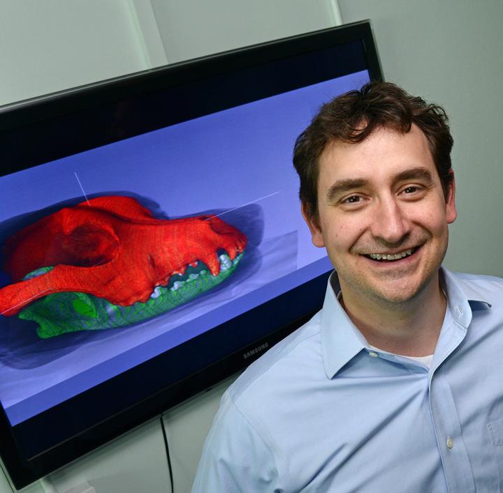 Jeff Schoenebeck standing in front of a 3D picture of a dog skull.
