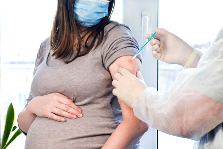 Pregnant woman being vaccinated against covid-19 while wearing a facemask 