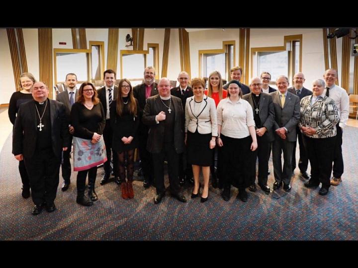 Divinity student Rachel Frost standing among Scottish Church reps and the First Minister inside the Scottish Parliament