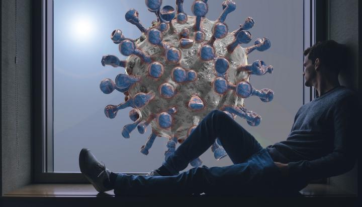 A man sits on the floor, looking towards a large virus particle
