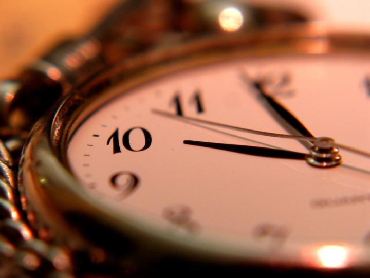 An up close photograph of a gold pocket watch clock face. The hands of the watch are pointing to 10 o'clock