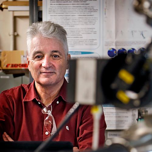 Professor Ian Main smiles to camera with lab equipment in the foreground out of focus
