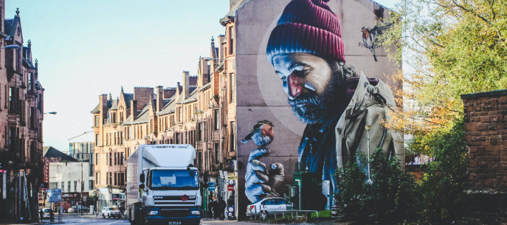 Glasgow city street, with one of the buildings covered in large artistic graffiti of a bearded man with a robin on his finger