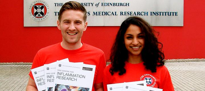 Two young medical researchers holding leaflets about the MRC Centre for Inflammation Research