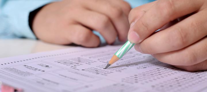 Photograph of a person's hands on a table answering exam questions. The person is holding a pencil and marking his answers on th