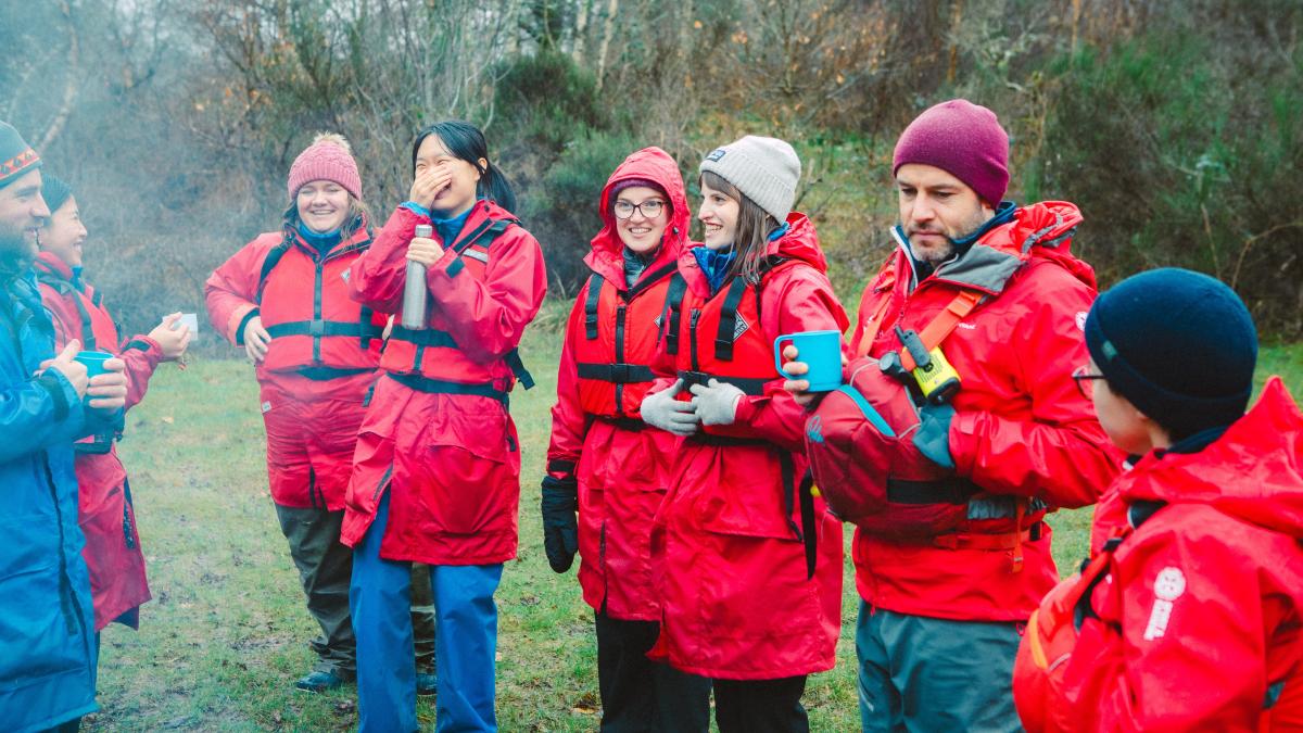A group or students and staff, wearing red jackets, attending a nature-based learning course at Firbush, the University of Edinburgh's outdoor education centre in Perthshire