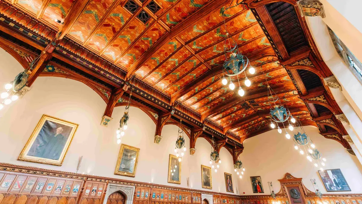 An upwards looking interior view of the intricate and colourful ceiling of the Rainey Hall at New College