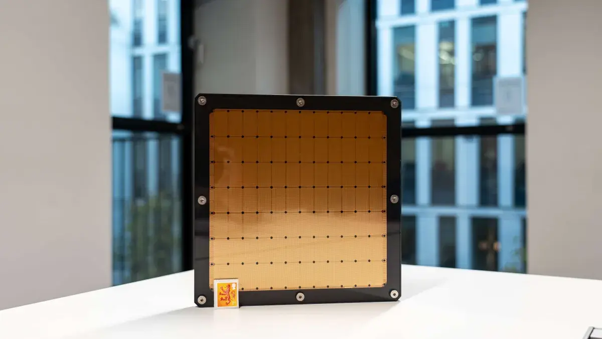 A photograph of a Cerebras AI chip sitting on its side on a white table with a postage stamp in front of it to provide scale. The postage stampe is about 1 per cent the size of the AI chip.