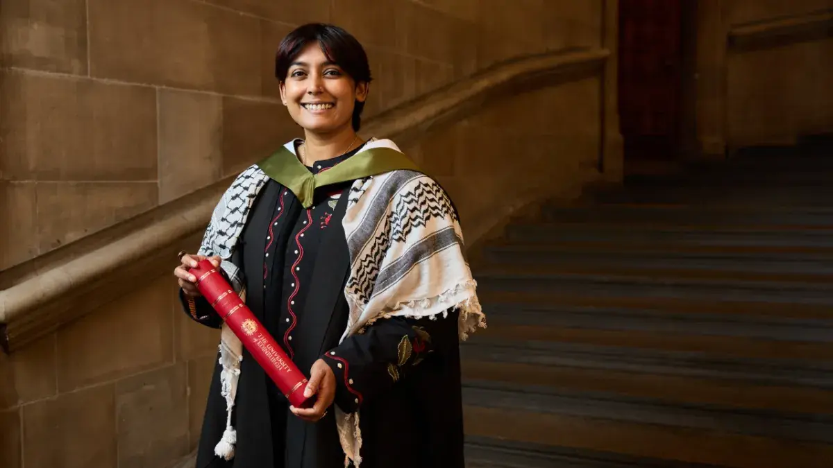Student Shakya Seresinghe picture with their degree on the stone staircase inside McEwen Hall.