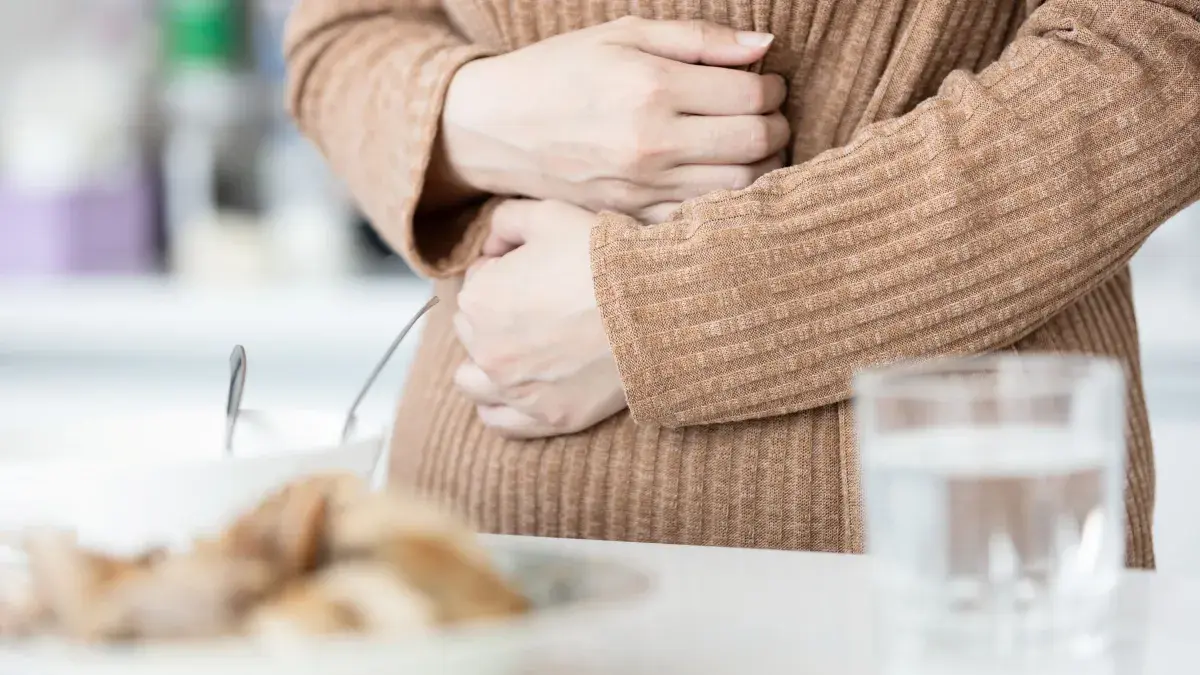 Close up of woman wearing beige jumper holding stomach