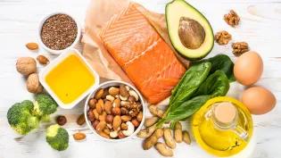 Keto diet food products displayed on a white wooden table. Salmon, olive oil, avocado, eggs, nuts and vegetables.