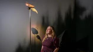 A woman looks up at a sculptural lamp which is part of her exhibition.