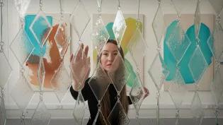 An ECA graduate approaches a sculpture that they designed made of glass and steel.