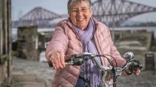 Joyce Faulkner on a bike in front of the Forth Railway Bridge, South Queensferry