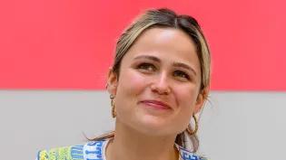 Graduating student Poppy Morgan wearing a blue and yellow collar in front of a pink backdrop with a white collar suspended in front of it