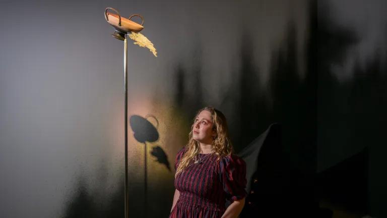 A woman looks up at a sculptural lamp which is part of her exhibition.