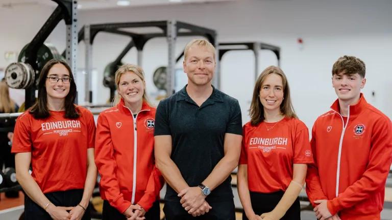 Sir Chris Hoy pictured centre, with four sports scholars wearing red University of Edinburgh sportwear