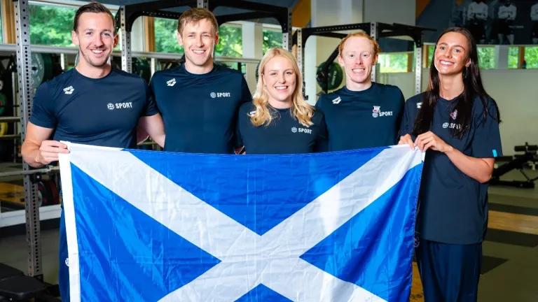 A group of swimmers from the University stand in a group holding a Scottish flag