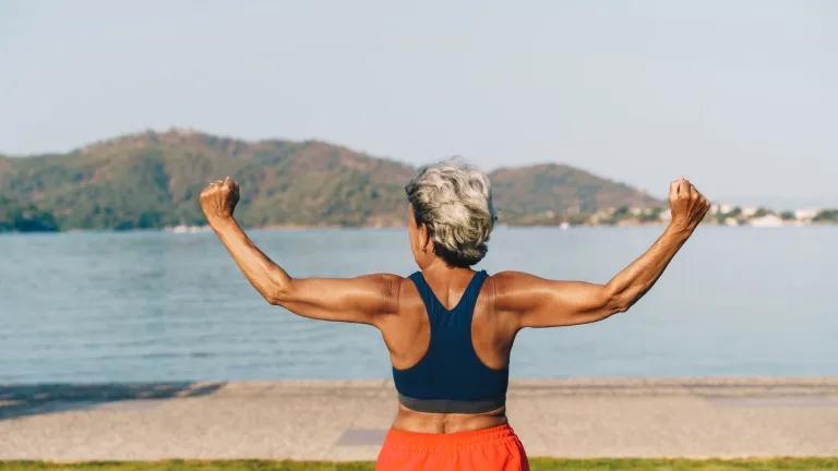Senior woman pictured from behind exercising her back outdoors in a park