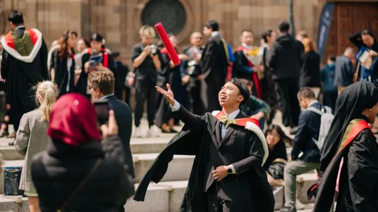 A student throwing his graduation scroll in the air outside McEwan Hall during the 2024 summer Graduations