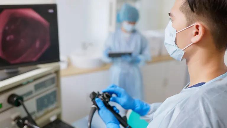 Doctor wearing protective mask holding endoscope looking at camera screen