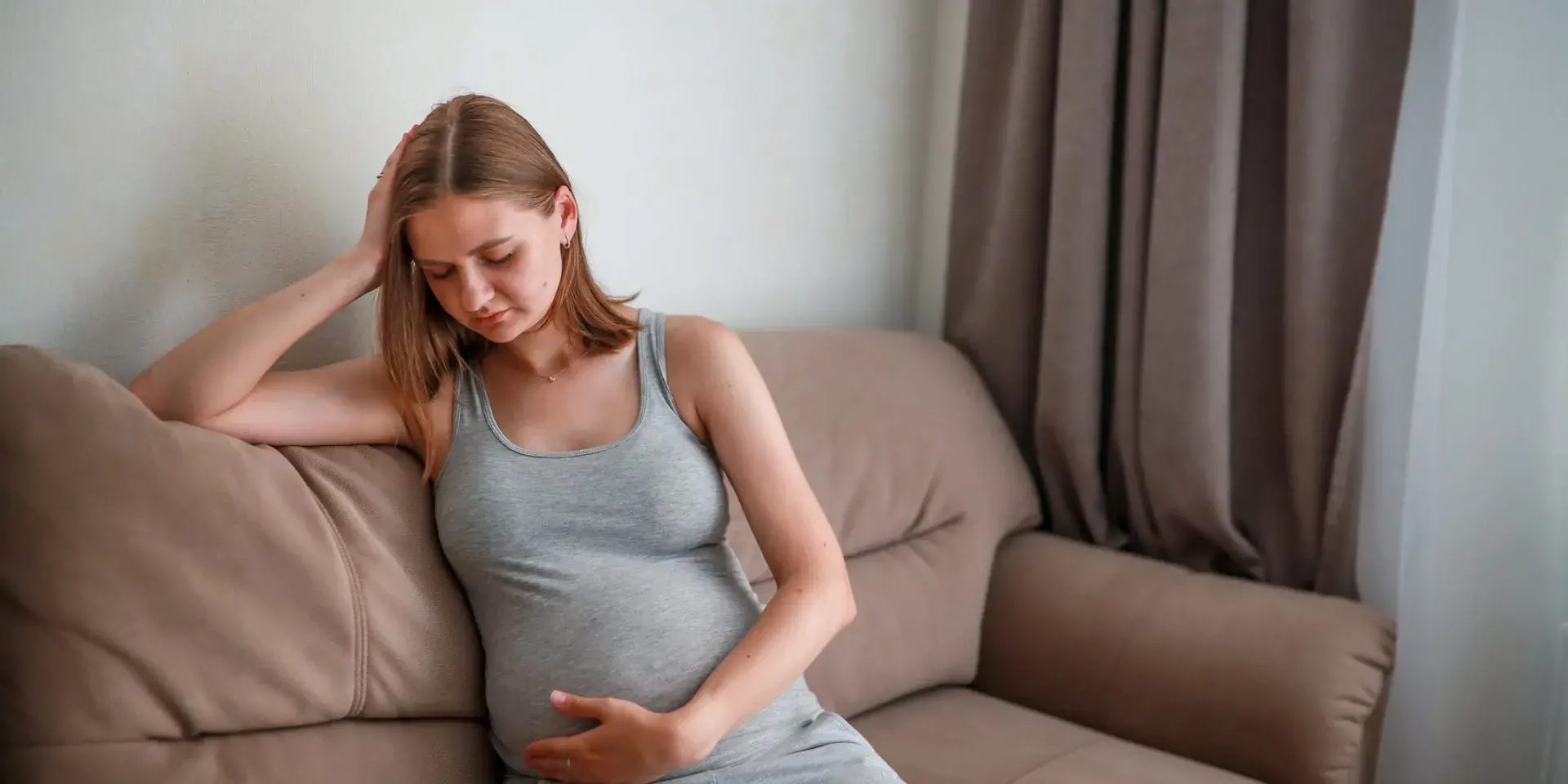 A pregnant woman sits on a sofa looking in some discomfort