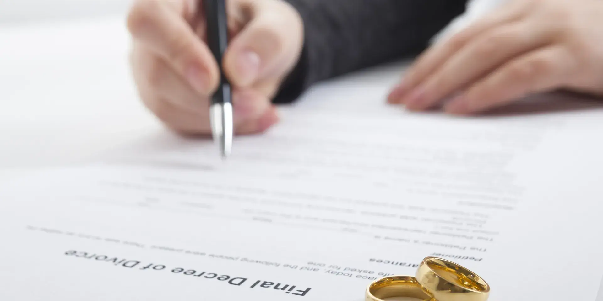  A person signs a divorce document. Two gold wedding rings are on the document