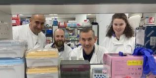 Four members of the REACT Edinburgh team pictured in the lab wearing white lab coats with lab materials in the foreground
