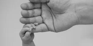 A baby's hand is seen gripping its mother's little finger