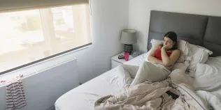 A teenage girl lies in bed looking out of the window