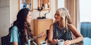Two women sitting at a table and talking while drinking coffee
