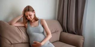 A pregnant woman sits on a sofa looking in some discomfort