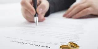  A person signs a divorce document. Two gold wedding rings are on the document