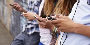 Group of four teenagers standing a line looking at mobile phones