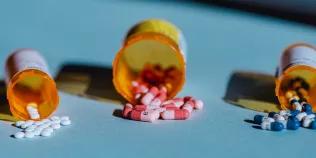 Three containers lie open on a table with pills spilling out of them