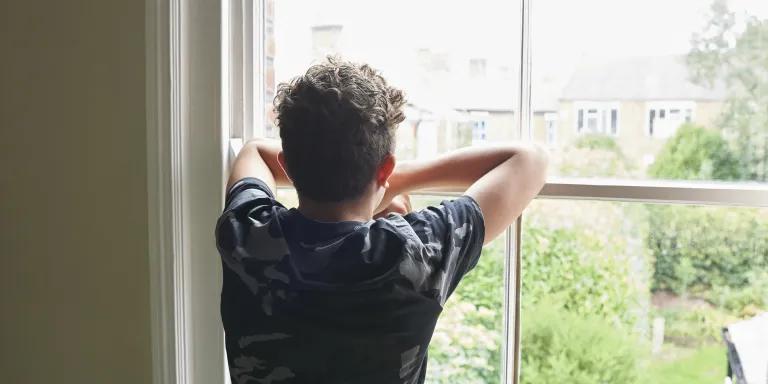 Teenage boy wearing dark t shirt looking out of bedroom window