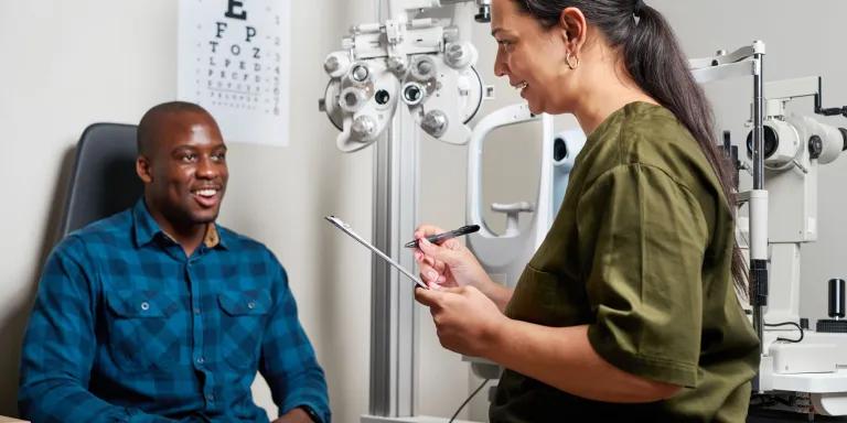 A patient and an optometrist sharing a positive interaction during an eye examination in a modern clinic, with an eye chart and testing equipment in the background.