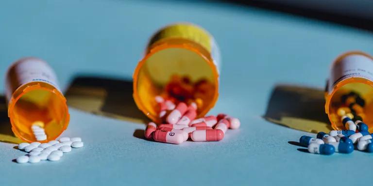 Three containers lie open on a table with pills spilling out of them