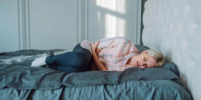A woman in pain lying on bed and holding her stomach.
