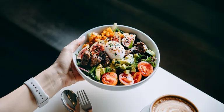 Close up of woman's hand holding a bowl of fresh, healthy food.