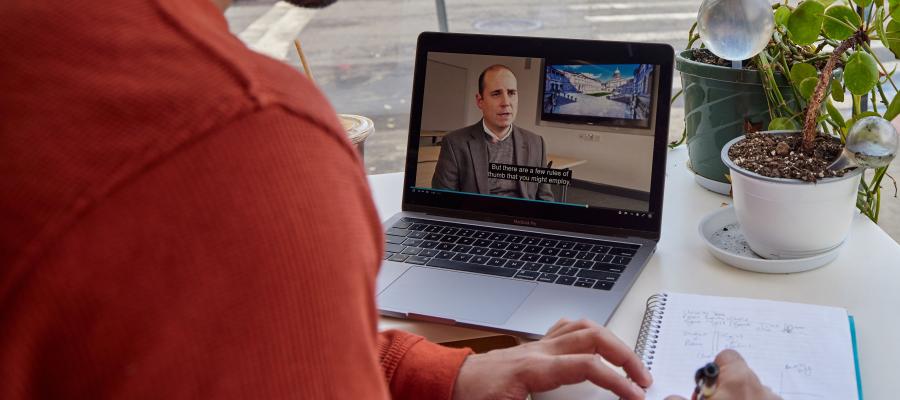 Someone watches a video on their laptop while taking notes