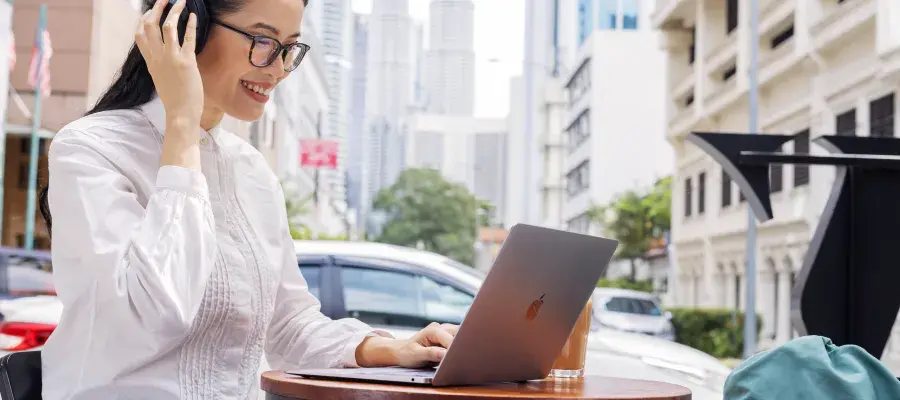 Female student smiling while using laptop and adjusting headphones in Kuala Lumpur