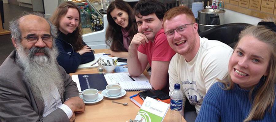 6 people sit around a table and smile to camera