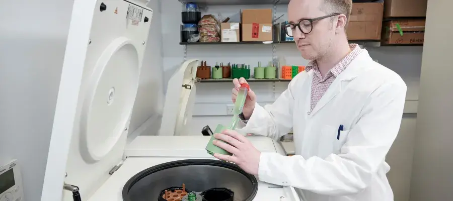A man in a laboratory wearing a white coat transferring liquid between two containers