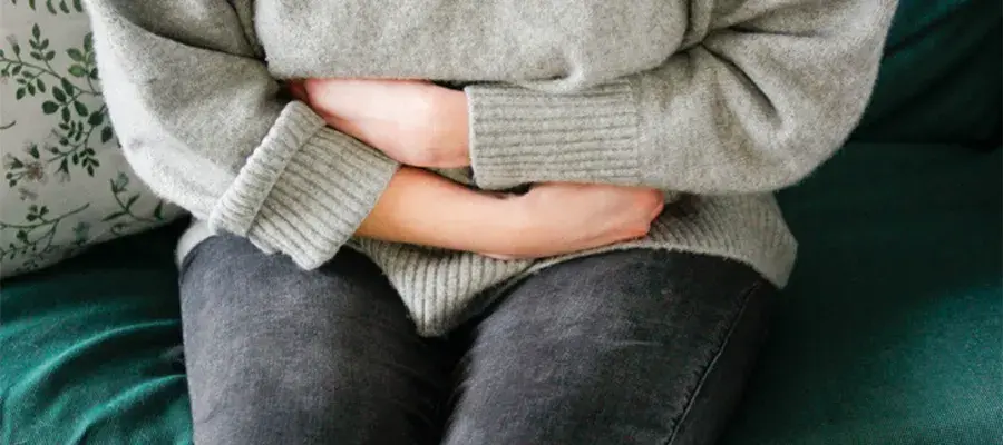 A person sat on a sofa with their arms crossed on their midriff in pain.