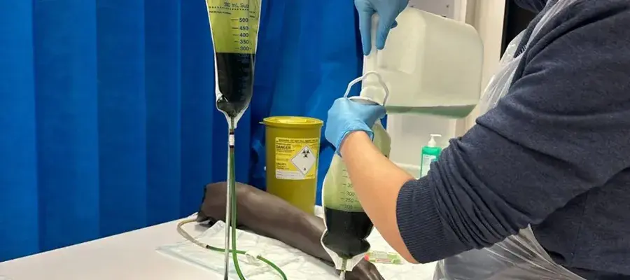 A person in a clinical setting pouring green blood into a bag